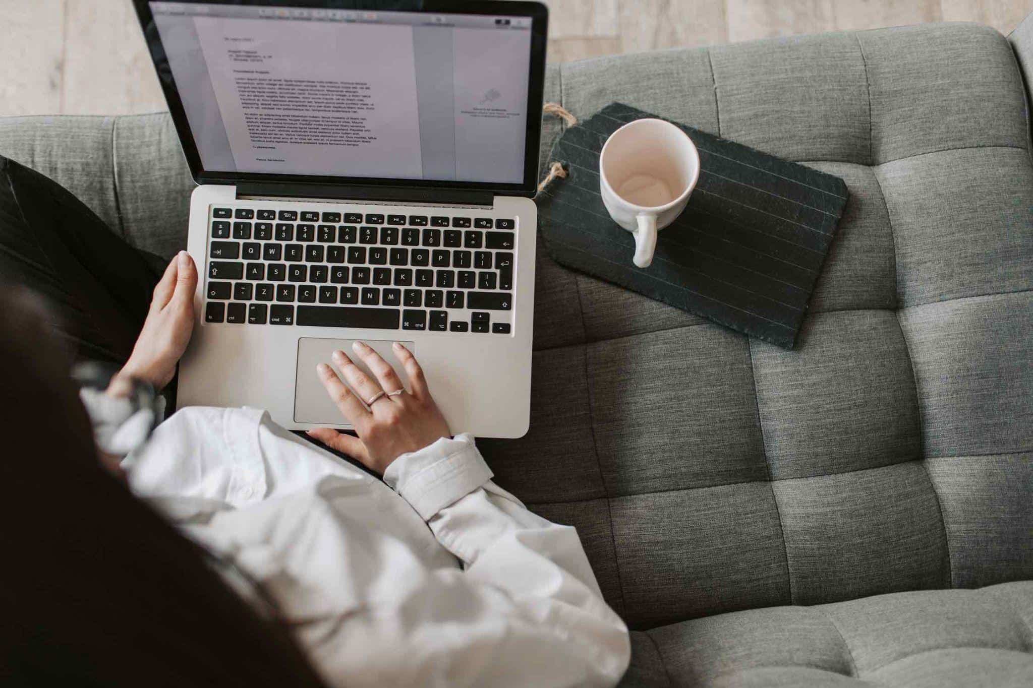 Woman sitting on a couch writing on a laptop with a coffee