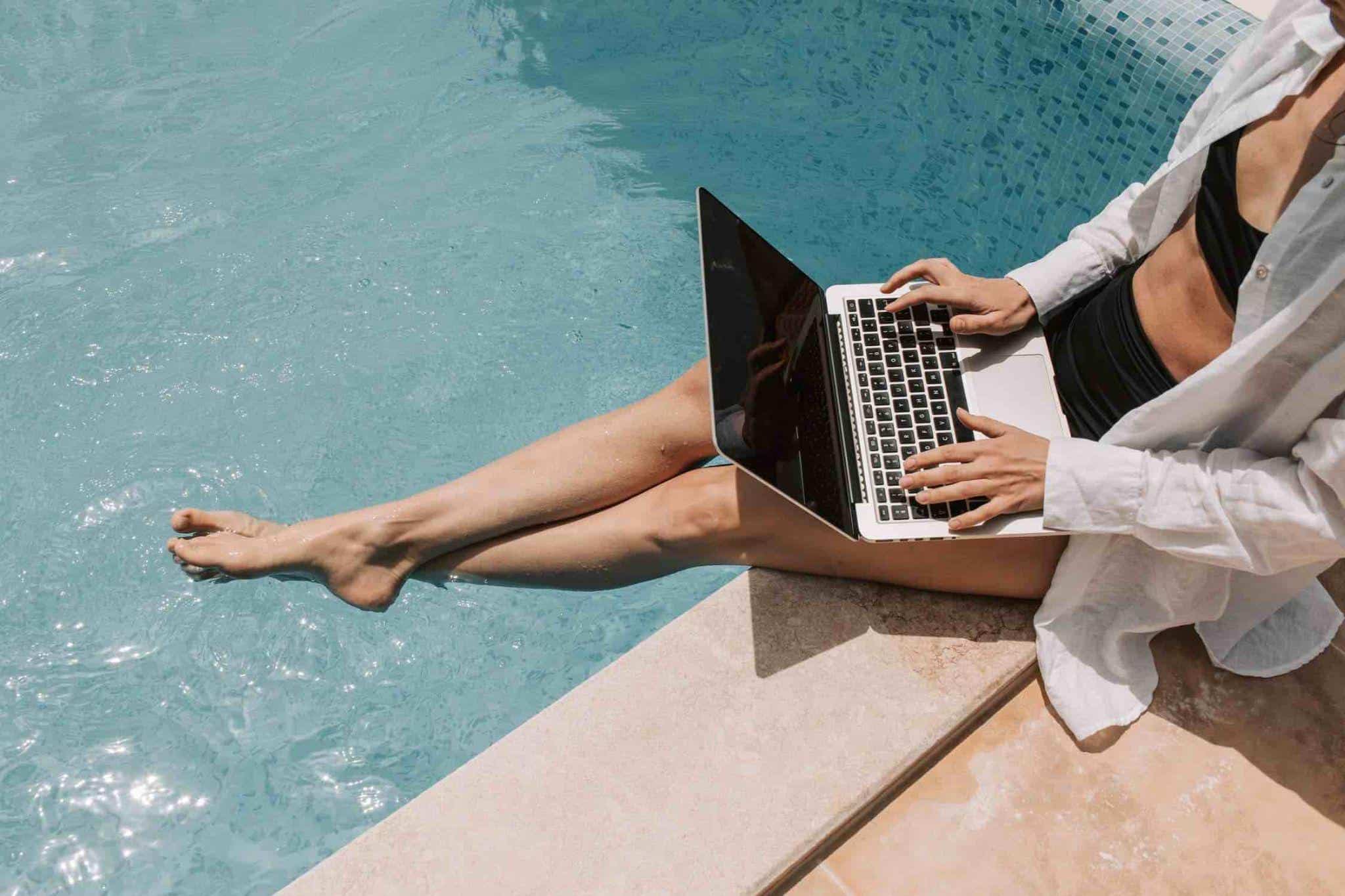 woman sitting by a pool with a laptop