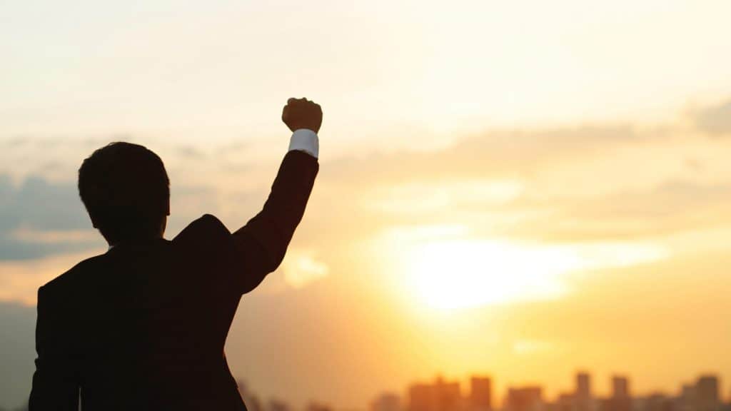 Silhouette of a Man with a raised fish looking into the sun and city skyline celebrating success